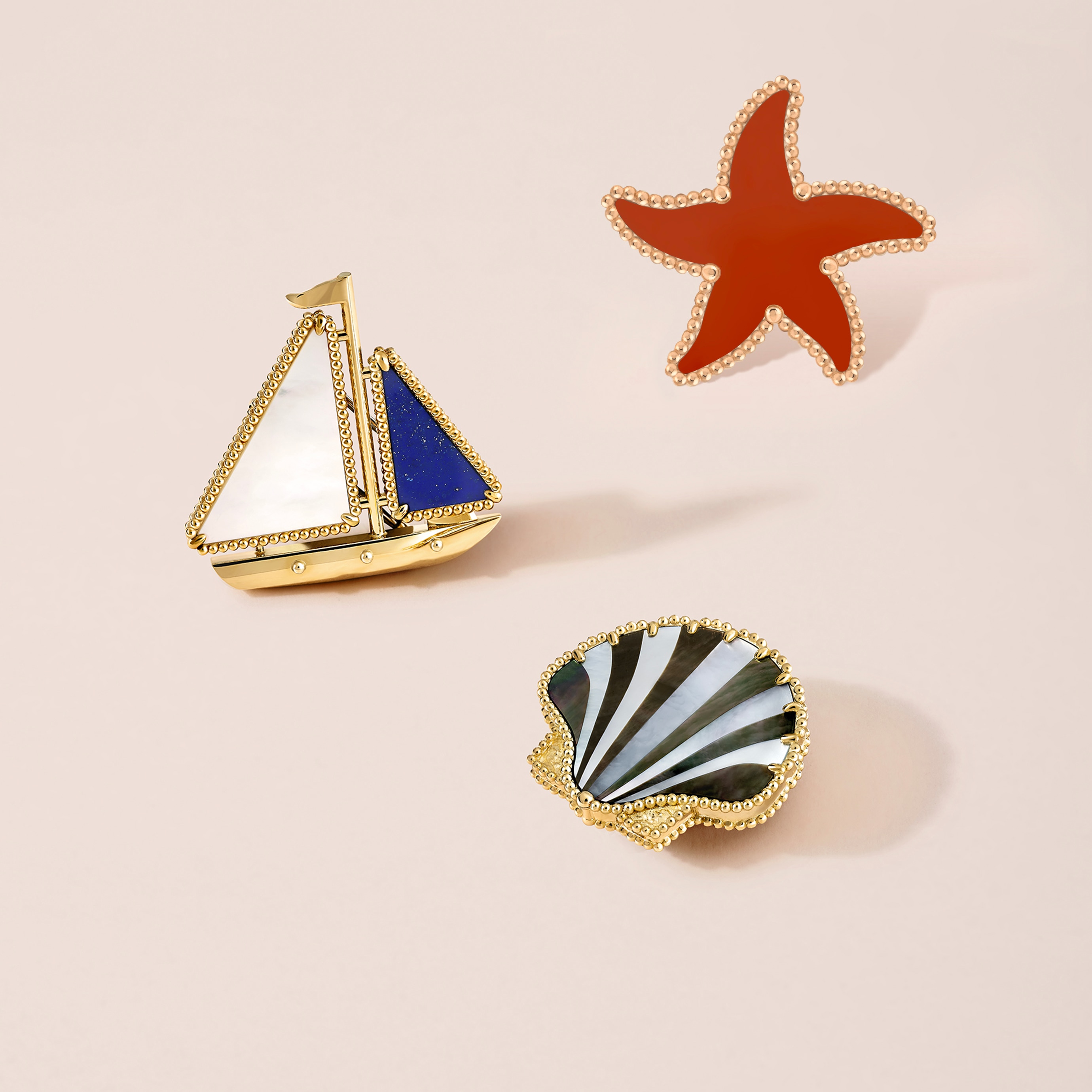 Clip Estrella de mar, oro rosa, jaspe rojo; clip Barco, oro amarillo, lapislázuli, nácar blanco; y clip Concha, oro amarillo, nácar blanco, nácar gris. Colección Lucky Summer, Van Cleef & Arpels.